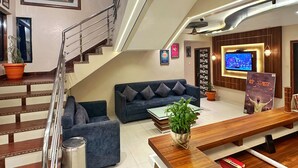 Un interior modern amb una escala, un sofà blau, una banca de fusta i una televisió penjada a la paret.