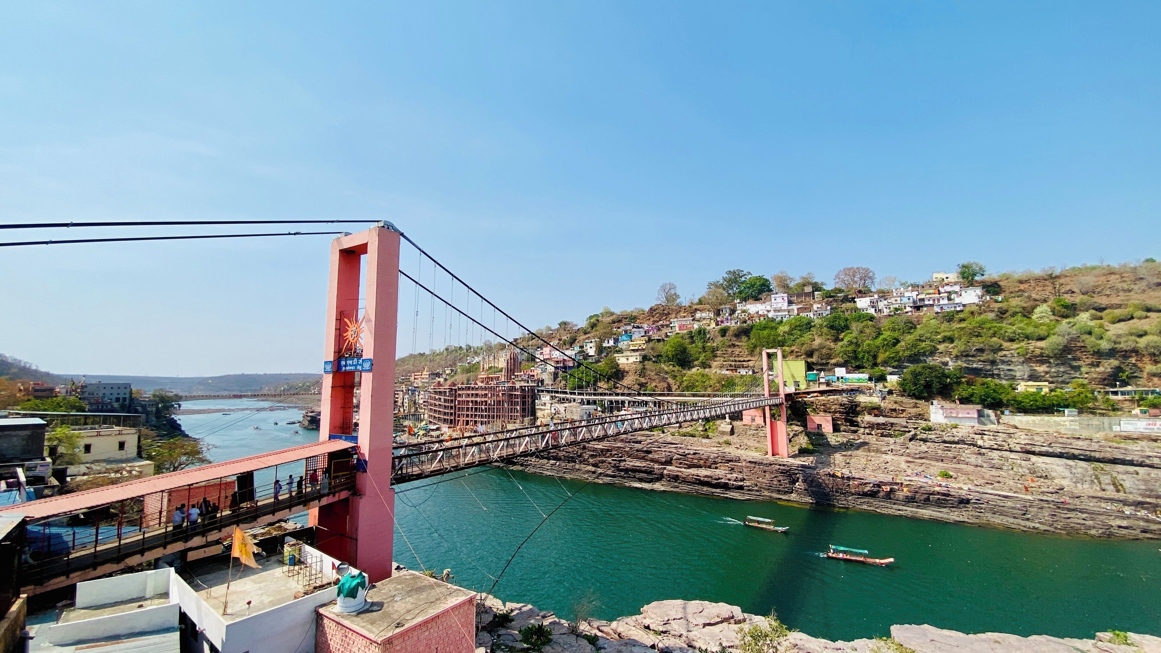 Un puente colgante sobre un río, con un pueblo al fondo.