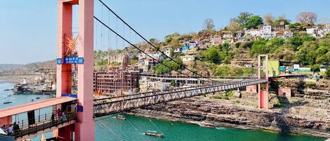 A bridge with a large tower and a river below. There are boats on the river and buildings on the opposite bank.