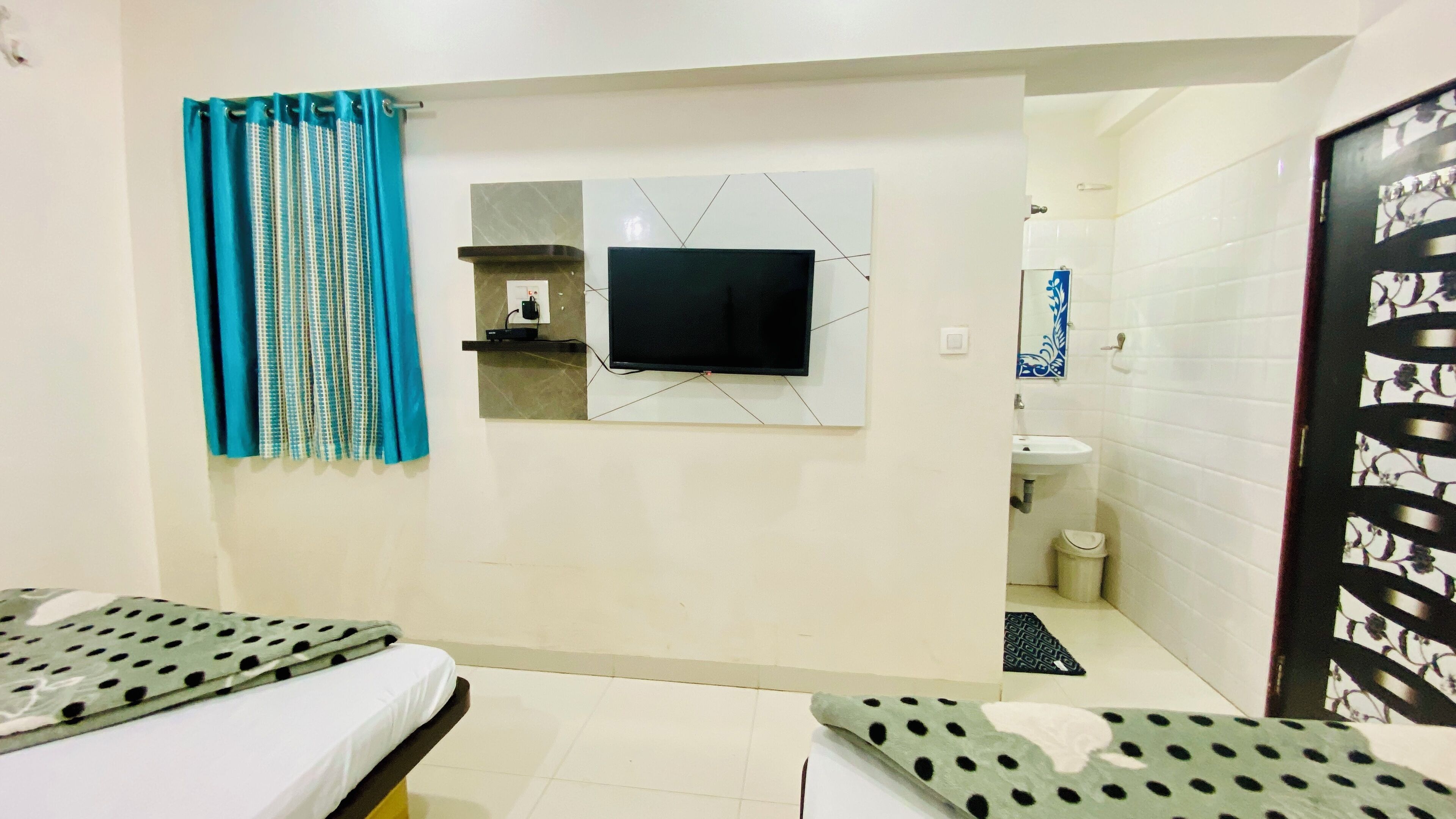 A hotel room with a bed, a TV mounted on the wall, a bathroom with a sink and toilet, and a patterned door.