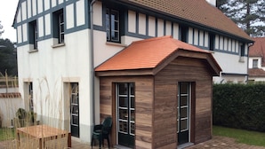 Une maison à deux étages, dotée d’une façade distinctive à pans de bois et d’une petite extension en bois avec de grandes fenêtres.