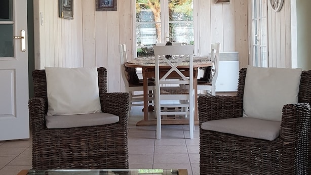 Une pièce meublée de meubles en osier, avec une table basse en verre et un coin repas comprenant une table et des chaises.