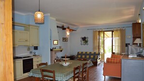 Un comedor con una mesa dispuesta para cuatro, una cocina con armarios y estufa, un sofá y un televisor.