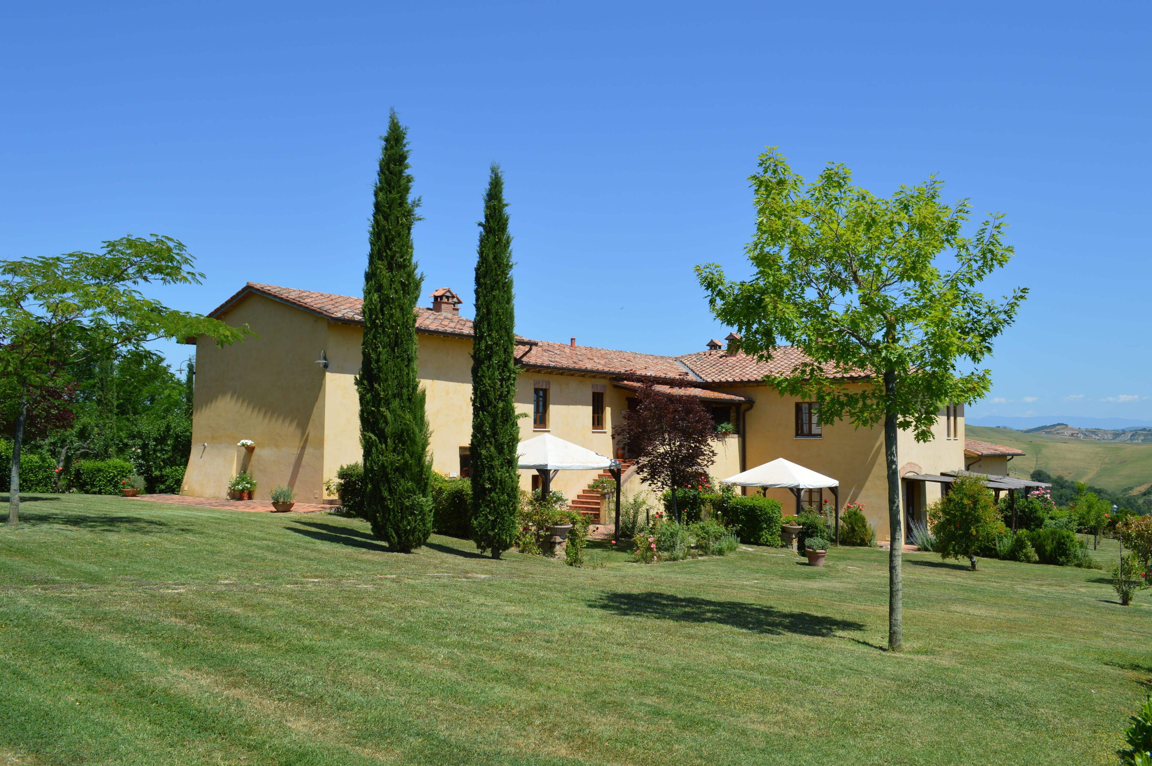 A two-story house with a tiled roof, surrounded by a well-maintained lawn and tall trees.