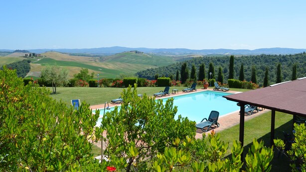 Una piscina con sillones de descanso, rodeada de vegetación y colinas al fondo.