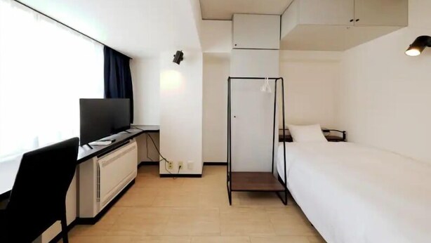 Quarto de hotel compacto com cama, escrivaninha com cadeira, televisão e guarda-roupa.