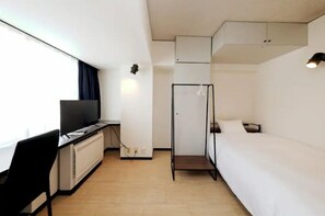 Une chambre d’hôtel de taille réduite, comprenant un lit, un bureau avec une chaise, une télévision et une armoire.