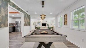 Sala de estar moderna com mesa de bilhar, cozinha ao fundo e área de jantar com televisão.
