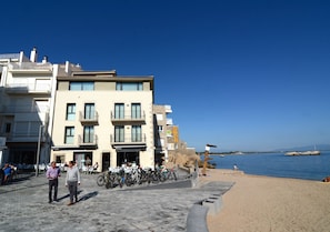 A coastal building with balconies, a paved walkway, and a beach in the background.