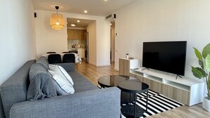Un salon moderne avec un canapé gris, un téléviseur à écran plat, une petite table ronde et une plante en pot.