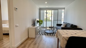 A compact living space with a bed, a sofa, a dining table, and a small kitchen area.