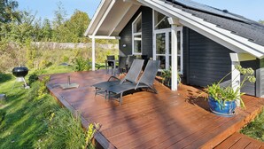 A modern house with a deck, a barbecue grill, and outdoor furniture.