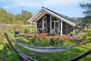 A modern house with a sloped roof, a patio with outdoor furniture, and a hammock in the foreground. - Lovely summer house with Spa close to the beach (Vejby)