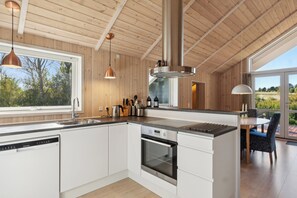 Eine moderne Küche mit Holzwänden, einem eingebauten Backofen, einer Spülmaschine und einem Essbereich mit Tisch und Stühlen.