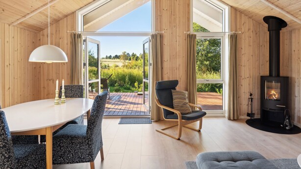A wooden interior with a dining table, chairs, a rocking chair, a fireplace, and large windows.