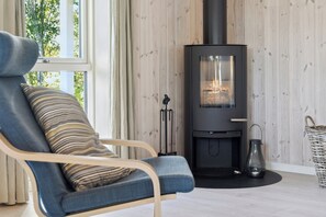 A room with a modern chair, a wood-burning stove, and a view through a window. - Lovely summer house with Spa close to the beach (Vejby)