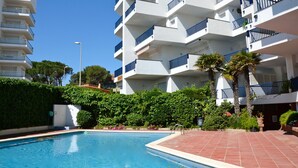 En modern lägenhetsbyggnad med en swimmingpool, balkonger och frodig grönska.