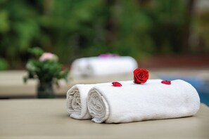 Two neatly rolled white towels with red rose petals on a beige surface, likely in a hotel setting. - Angkor Green Boutique (Siem Reap)
