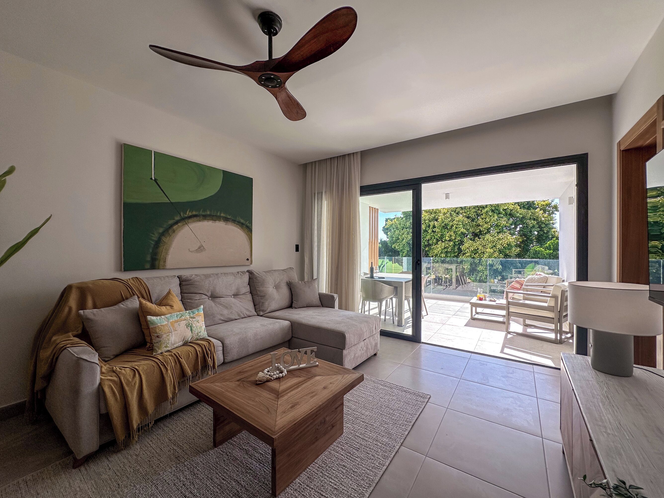 A modern living room with a sofa, a coffee table, and a ceiling fan. There is a sliding glass door leading to an outdoor patio area.