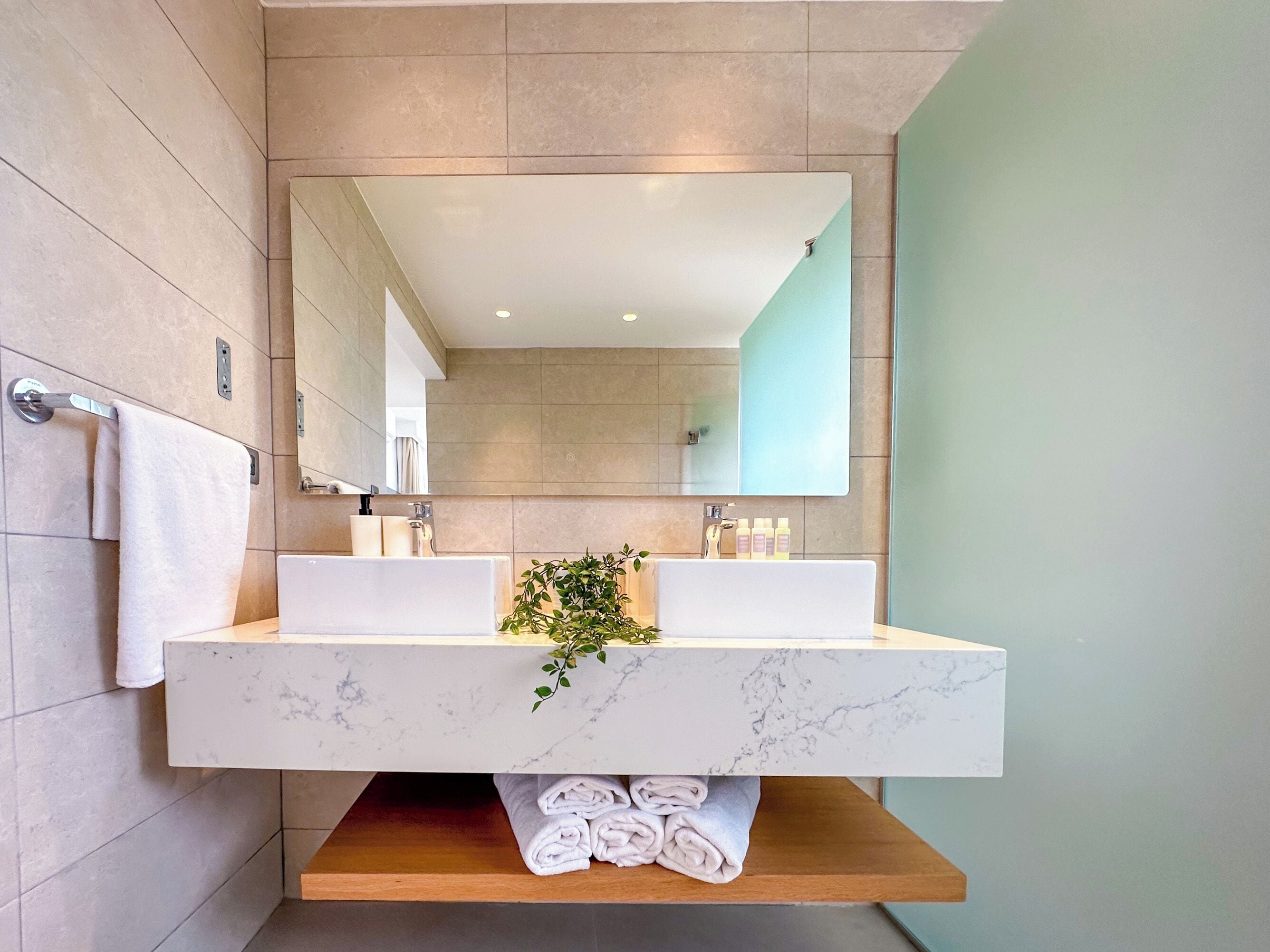 Un baño moderno con tocador de mármol, un espejo grande y un perchero.