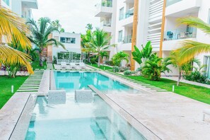Un hotel moderno con una piscina central, rodeado de exuberante vegetación y palmeras.