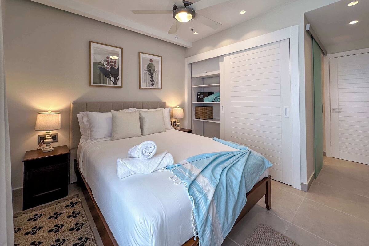 Un dormitorio ordenado con cama, lámparas de noche, ventilador de techo y armario empotrado.