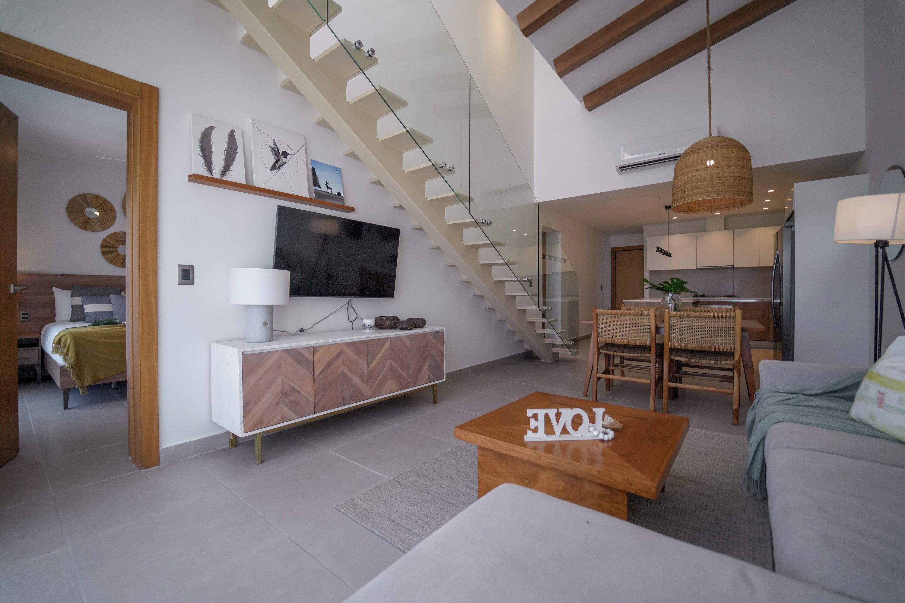 A modern living room with a staircase, a dining area, and a kitchen.
