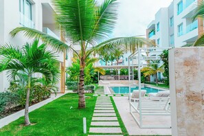 Un patio moderno de hotel con piscina, palmeras y una zona de descanso.