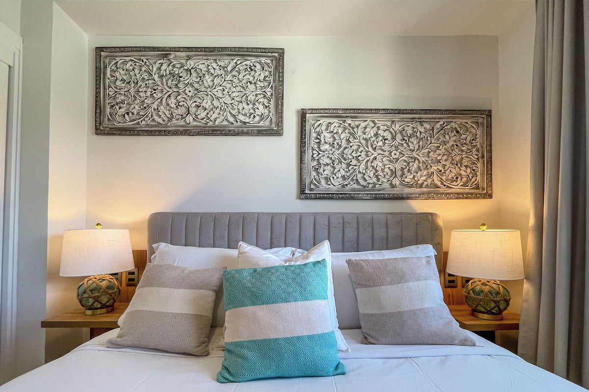 Una cama bien hecha con dos almohadas, dos lámparas de noche y dos elementos decorativos en la pared.