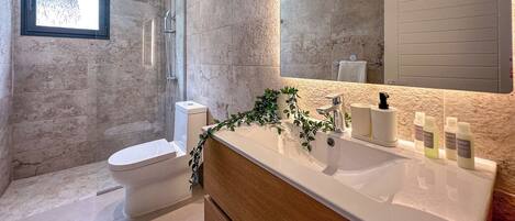 Un baño moderno con ducha, inodoro y tocador con espejo y artículos de aseo.