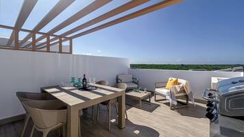 Una terraza en la azotea con una mesa, sillas, una parrilla y vistas al paisaje.