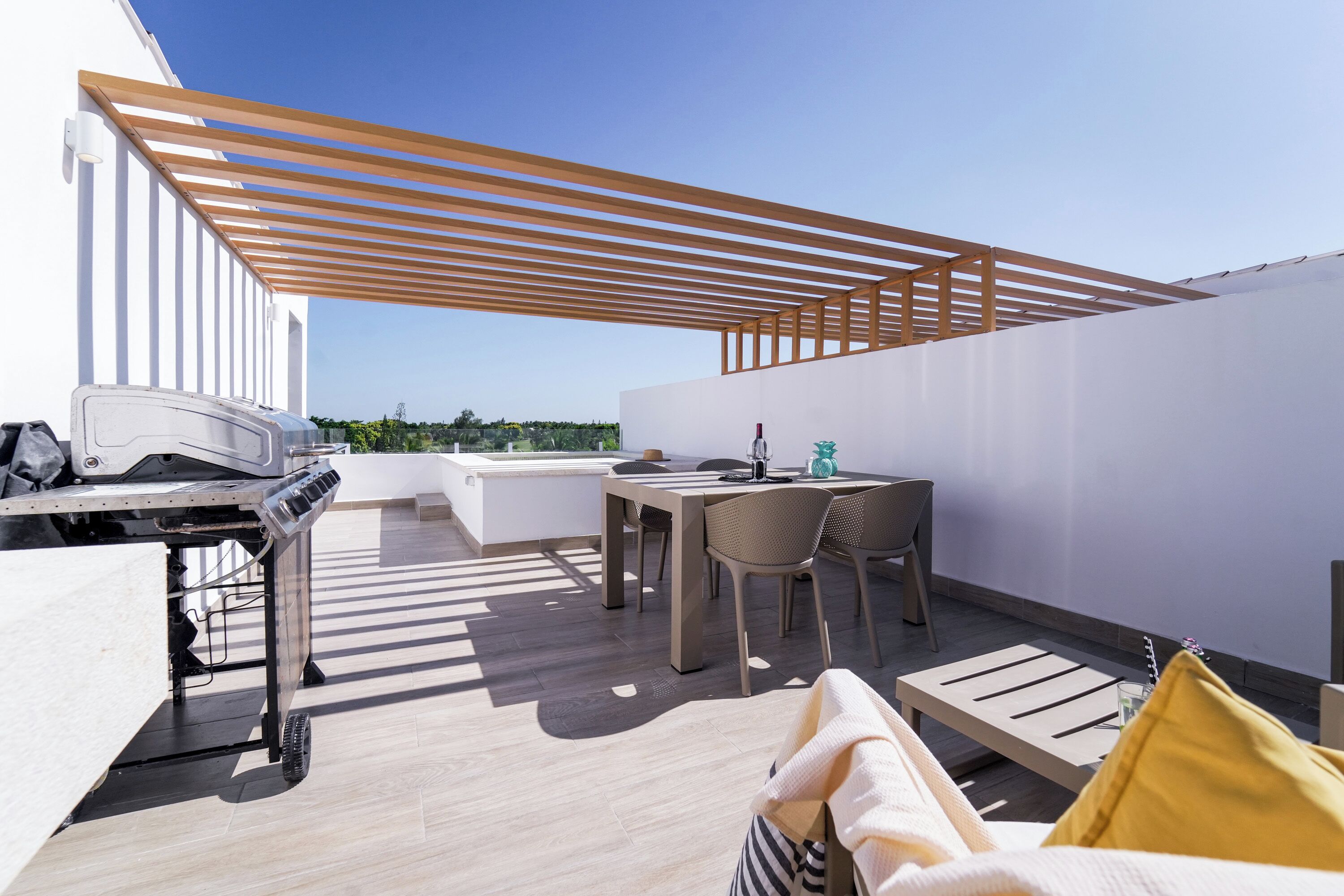 Une terrasse sur le toit avec une pergola en bois, une table à manger avec des chaises et un barbecue.