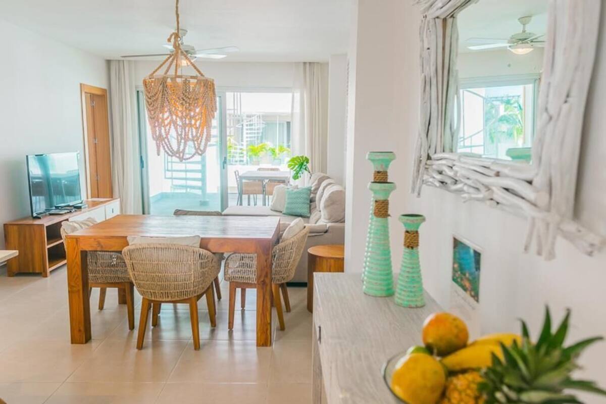 Una sala moderna con una mesa de comedor de madera, sillas de mimbre, un sofá y un ventanal con cortinas.