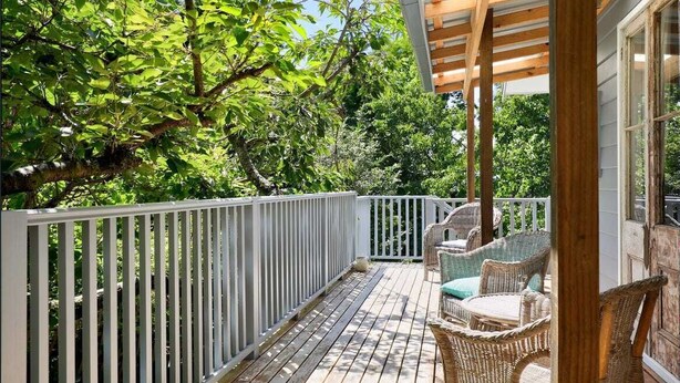 Una terraza de madera con mobiliario de mimbre y barandilla blanca.