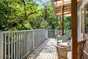 Una terraza de madera con mobiliario de mimbre y barandilla blanca.