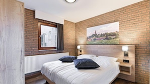 A modern bedroom with a brick wall, a large window, a painting, and a nightstand with a lamp. - South Limburg Stay Near Tripoint (Vijlen)