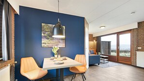 A dining area with a table and two orange chairs, a pendant light, and a large window with a view. - South Limburg Stay Near Tripoint (Vijlen)
