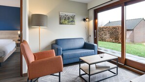 A modern hotel room with a bed, a blue sofa, an orange armchair, a coffee table, a lamp, and a painting on the wall. - Holiday Home Near Vijlen (Vijlen)