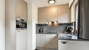 A compact kitchen with built-in appliances, a countertop sink, and a window with curtains. - Holiday Home Near Vijlen (Vijlen)