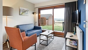 A modern living room with a blue sofa, orange armchair, and a small table with a remote control. - Holiday Home Near Vijlen (Vijlen)