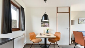 A dining area with a table, two chairs, a pendant light, a window with curtains, a radiator, and a door. - Holiday Home Near Vijlen (Vijlen)
