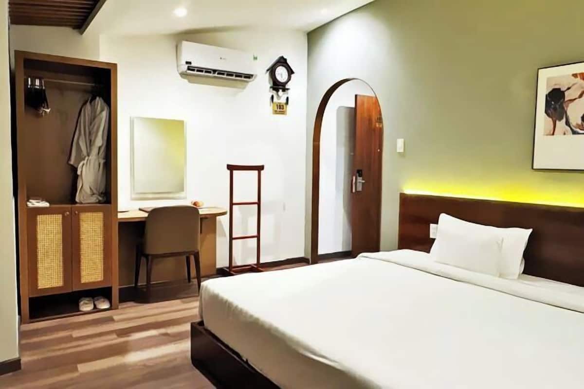 Ein Hotelzimmer mit Bett, Schreibtisch, Stuhl, Kleiderschrank, Klimaanlage und einer Wanduhr.