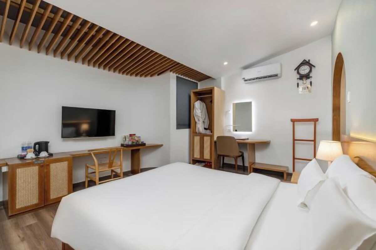 A hotel room with a bed, a desk with a chair, a television, a wardrobe, and a mirror.