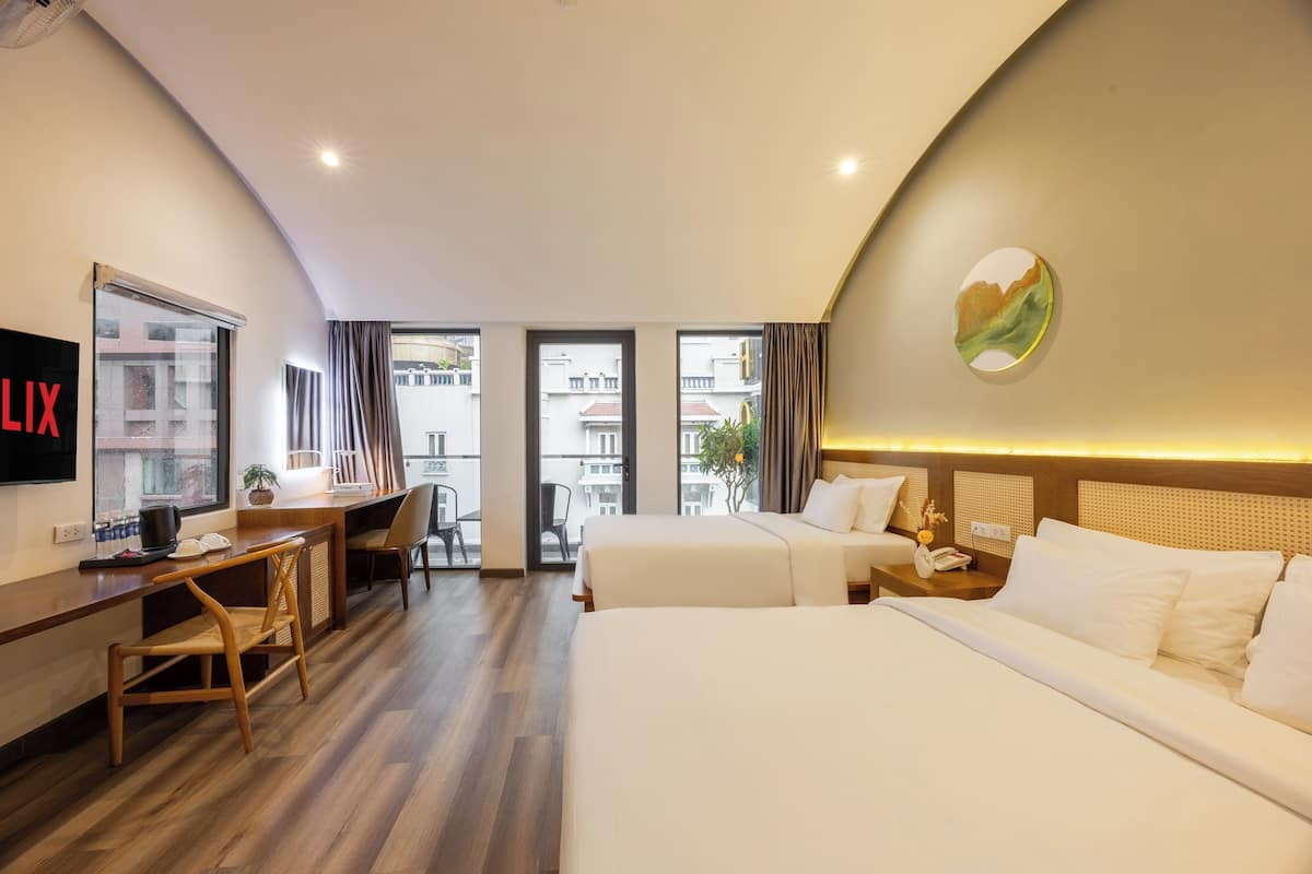 Ein Hotelzimmer mit zwei Betten, einem Schreibtisch, einem Stuhl, einem Fernseher und Blick auf die Stadt.