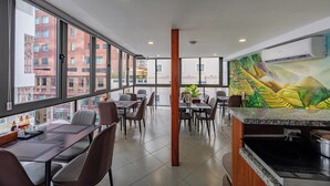 A modern restaurant with a view of buildings through large windows, a kitchen area, and a mural on the wall. - A25 Hotel - 14 Ho Huan Nghiep (Ho Chi Minh City)