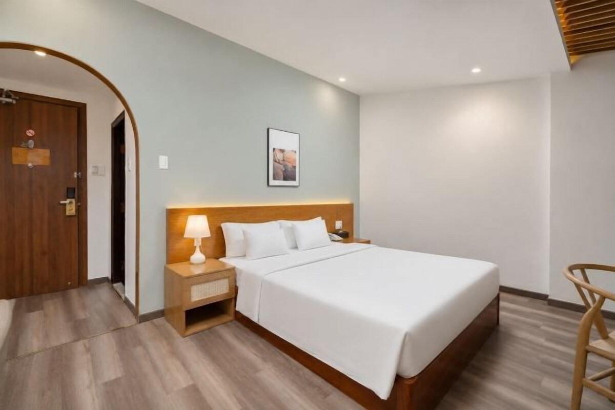 A hotel room with a bed, a nightstand with a lamp, a wooden door, and a small table.