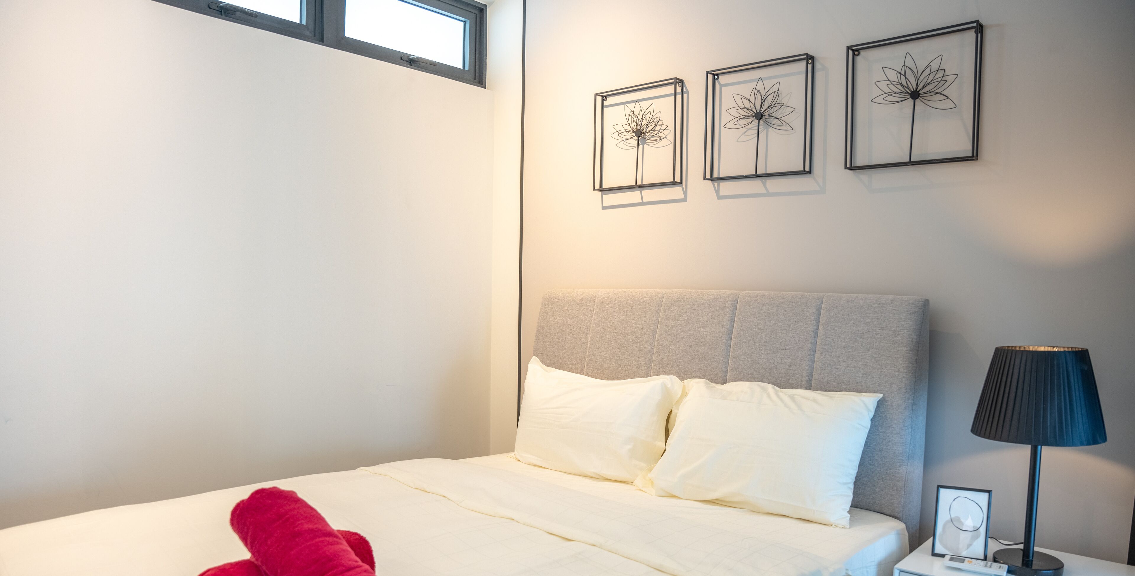 Une chambre à coucher avec un lit, des oreillers, une table de chevet avec une lampe et trois œuvres d’art encadrées accrochées au mur.