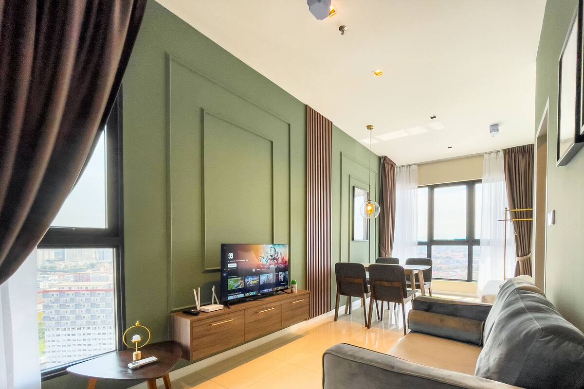 A modern living room with a flat-screen TV, a sofa, a dining table with chairs, and a view of a cityscape through large windows.