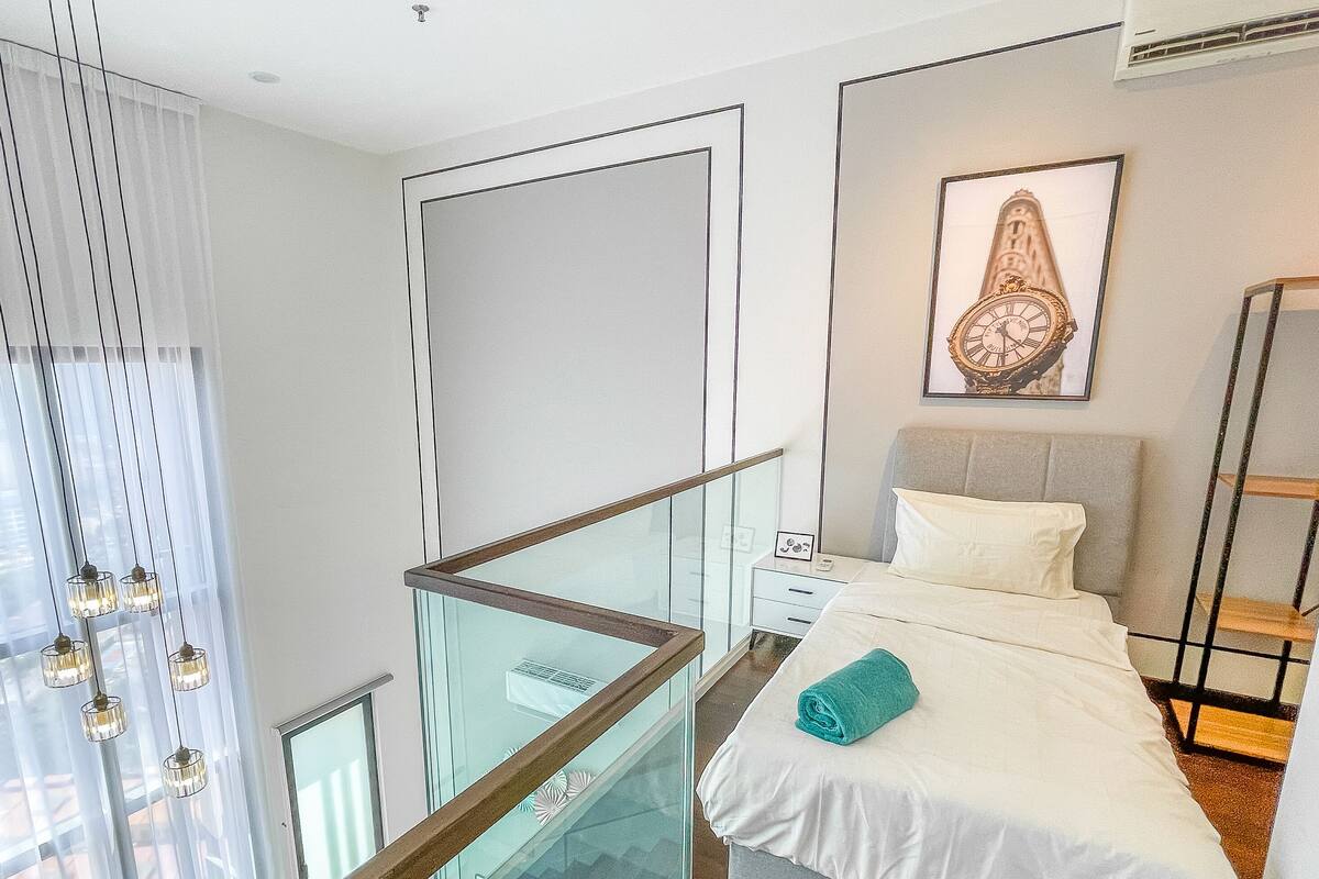 A modern hotel room with a balcony, a bed with a rolled towel, a framed clock on the wall, and a glass railing.