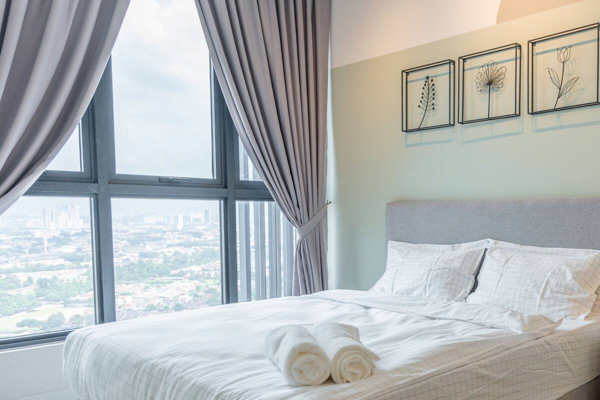 A hotel room with a bed, a nightstand, a lamp, and three framed floral artworks on the wall.